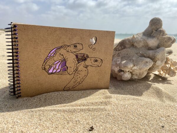 pink notebook with turtles and hearts on the sand
